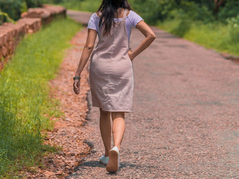 Walking young woman holding right lower back in pain